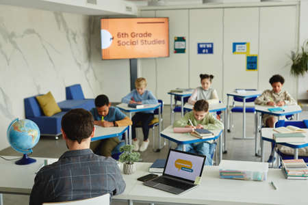 Wide angle view at school classroom with diverse group of children taking test, male teacher in foreground, copy spaceの写真素材