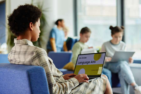 Side view portrait of young black girl using laptop and watching lesson on Language arts online,...