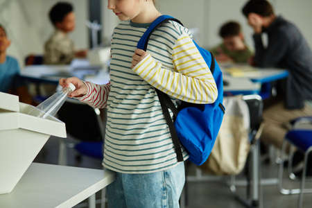 Side view of child using waste sorting bins in school and putting plastic bottle in for recycling, copy spaceの写真素材