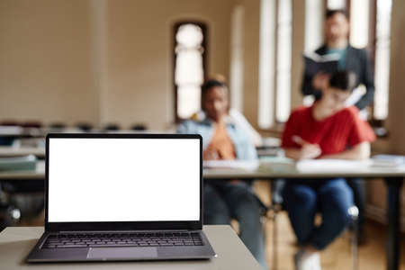 Background image of blank white laptop screen on table in college classroom, copy spaceの写真素材