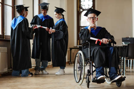 Full length portrait of young man with disability at graduation ceremony in university, copy spaceの写真素材
