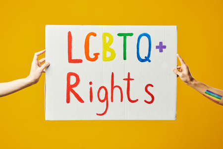 Vibrant shot of two hands holding LGBTQ rights sign against yellow backgroundの写真素材
