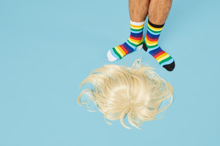 Minimal shot of man wearing rainbow socks with blond wig on floor at pastel blue background, copy spaceの写真素材