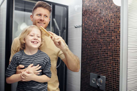 Portrait of happy father brushing hair of little boy and looking in mirror, copy spaceの写真素材