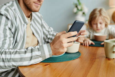 Close up of father using smartphone at dining table with little boy in background, copy spaceの写真素材