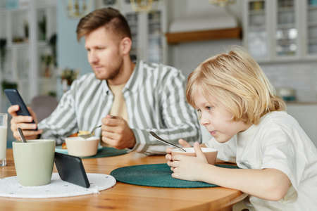Side view portrait of father and son using smartphones at dining table and watching videos, copy spaceの写真素材