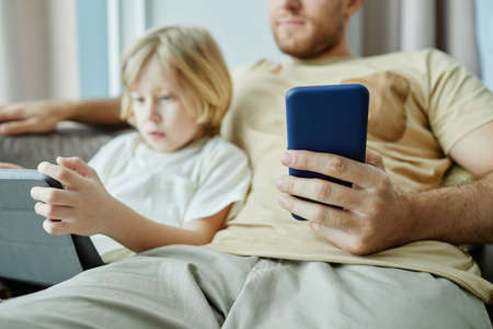 Close up of father holding smartphone with little boy using tablet in background, copy spaceの写真素材