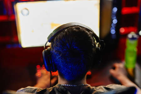 Back view at man playing video games in dark, focus on head with headphones, copy spaceの写真素材