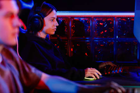 Side view portrait of young woman playing video games with cyber sports team in neon light, copy...