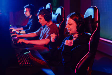 Side view portrait of young woman cheering while playing video games in cyber sports club and...