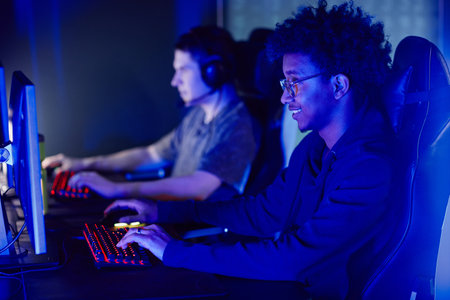 Side view portrait of smiling African American man playing video games in cybersports club in blue...