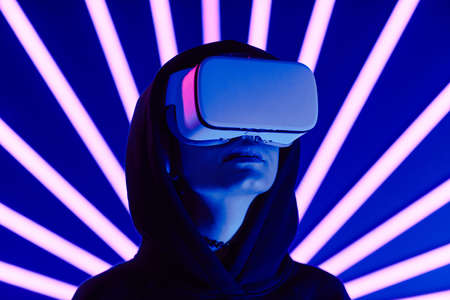 Futuristic shot of young woman wearing VR headset with neon light beams in background, copy spaceの写真素材