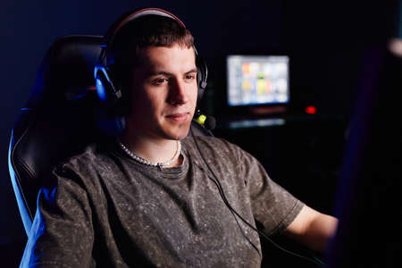 Portrait of Caucasian young man playing video games in dark and speaking into headset