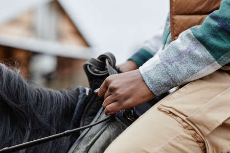 Closeup of young African American woman riding horse and holding onto reins gentlyの写真素材