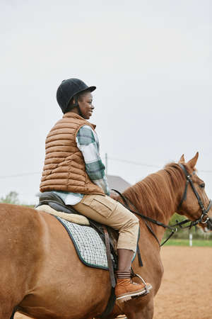 Vertical back view at young woman riding horse in ranch and wearing helmetの写真素材