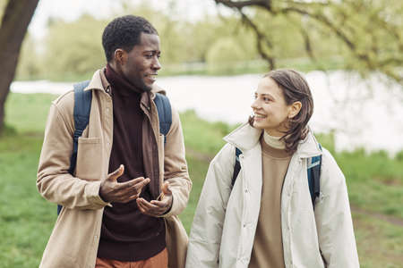 Happy multiethnic couple smiling to each other during conversation while they walking along the parkの写真素材