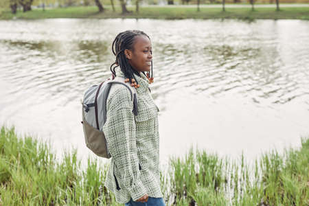 African teenage girl with backpack standing near the pond in the park spending time on fresh airの写真素材