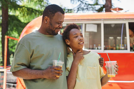 Happy father embracing his son while they walking outdoors and enjoying cold drinks during summer vacationの写真素材