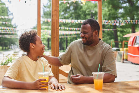Happy dad talking and laughing with his son while they drinking cold juice at table in outdoor cafeの写真素材