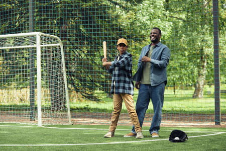 African happy dad learning his son to play baseball on the field outdoorsの写真素材