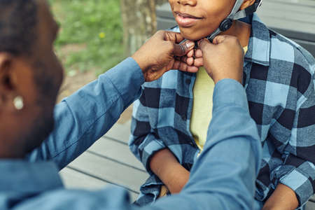 Close-up of father helping his son to wear the helmet before the outdoor gameの写真素材