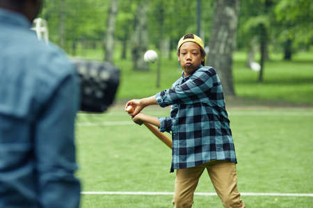 African boy learning to hit the ball with bat during game in baseball together with his dadの写真素材