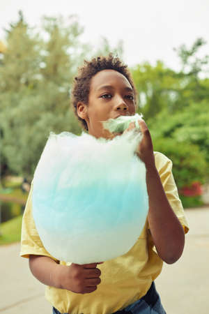African boy eating cotton candy while walking outdoors in the parkの写真素材