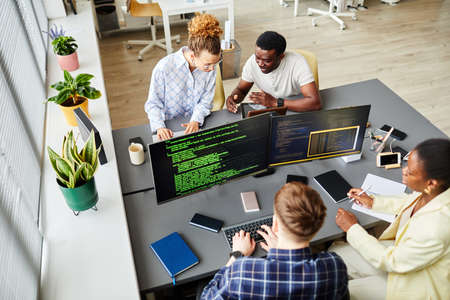 High angle view of programmers sitting at table with computer monitors and writing codes in team at officeの写真素材