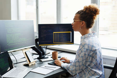 Young female IT specialist writing codes of new software on computer while sitting at her workplace at officeの写真素材