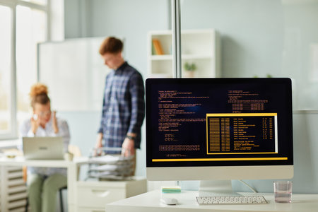 Close-up of computer codes of new software on monitor standing on office desk with programmers...