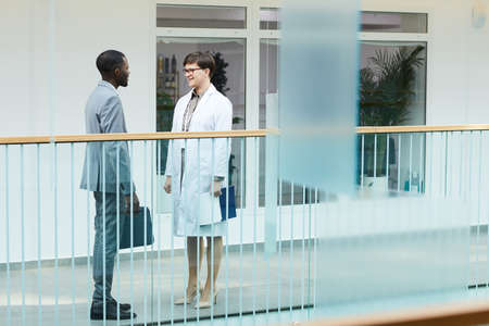 Full length shot of two people, man and woman chatting while standing at balcony in modern office...
