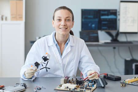 Portrait of smiling young woman as female engineer looking at camera while working in lab, copy...
