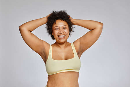Minimal waist up portrait of carefree black woman wearing underwear and laughing happily against...