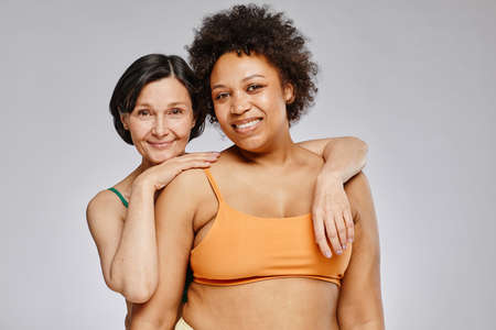 Minimal waist up portrait of two real women wearing underwear and smiling at camera against grey backgroundの写真素材