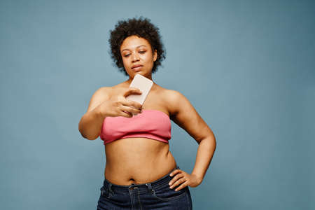 Waist up portrait of confident black woman taking selfie photo against pastel blue background, copy spaceの写真素材