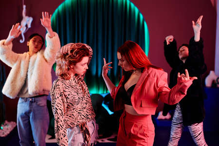 Side view portrait of two girls in dance battle challenge at nightclub lit by red neon lightsの写真素材