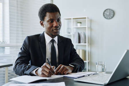 Portrait of successful black businessman writing in planner while managing finances for company,...