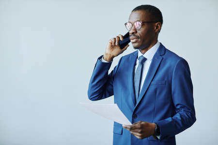 Waist up portrait of professional African American businessman speaking on phone in office, copy...
