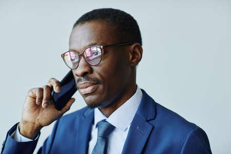Close up portrait of professional African American businessman speaking on phone against white...