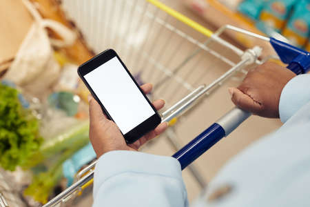 Close up of unrecognizable black woman buying groceries in supermarket and using smartphone with white screen mockup, copy spaceの写真素材