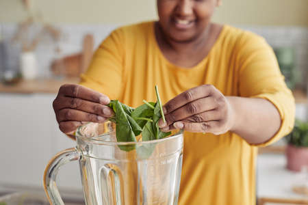 Close up of young black woman putting spinach in blender while making healthy smoothie at home, copy spaceの写真素材