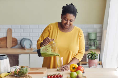 Portrait of overweight black woman enjoying healthy smoothie at home kitchen, copy spaceの写真素材