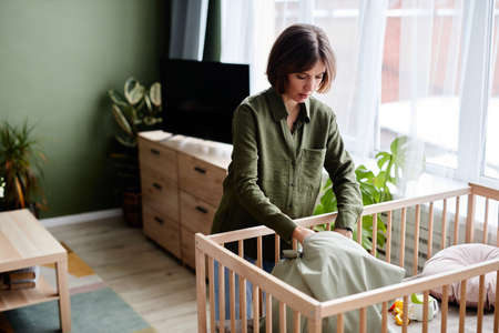 Portrait of young pregnant woman preparing baby crib at home, copy spaceの写真素材