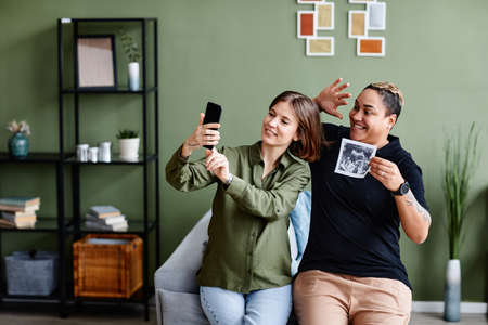 Portrait of young gay couple expecting baby and showing ultrasound image to family via video chat, same sex family lifestyleの写真素材