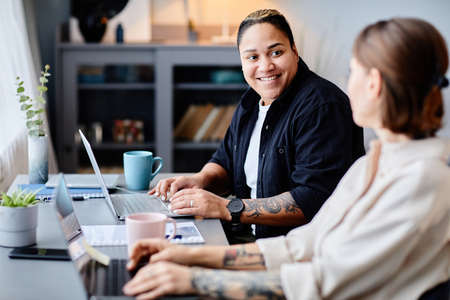Portrait of two modern women using computers at home workplace together and smiling, copy spaceの写真素材
