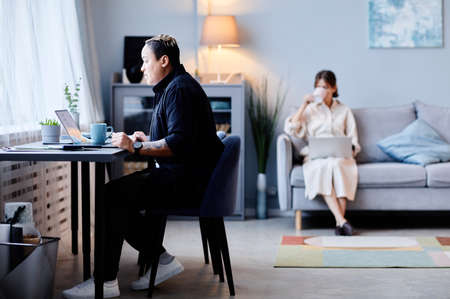 Minimal view at two young women at home, focus on person working at table in foreground, copy space