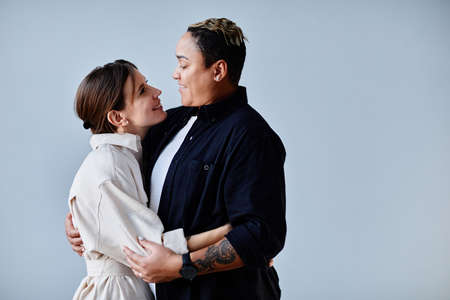 Minimal side view portrait of happy gay couple embracing against blue background, copy spaceの写真素材