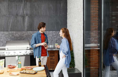 Wide angle view of two young people chatting while enjoying drinks at outdoor terrace party, copy spaceの写真素材