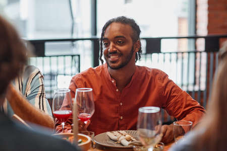 Portrait of young man talking to friends at table during dinner party in cozy settingの写真素材