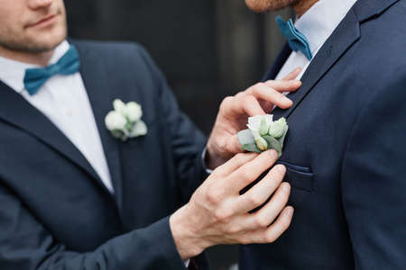 Close up of smiling young man fixing grooms boutonniere during wedding ceremony, same sex marriage conceptの写真素材